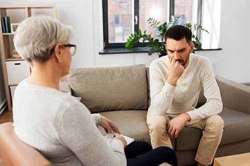 man sitting on a couch looking sad talking with therapist while in a treatment program
