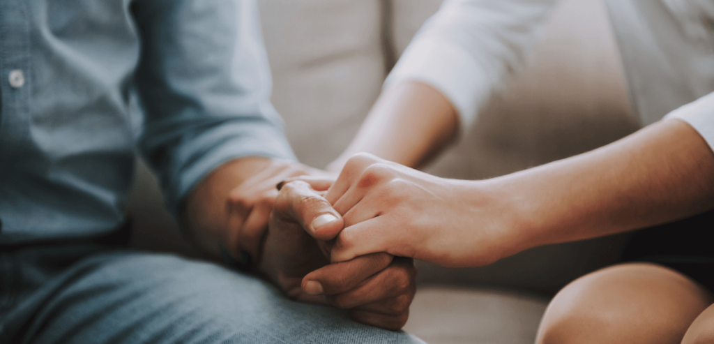 A closeup shot of a woman hands holding a man hand showing support while they are sitting on a sofa at home