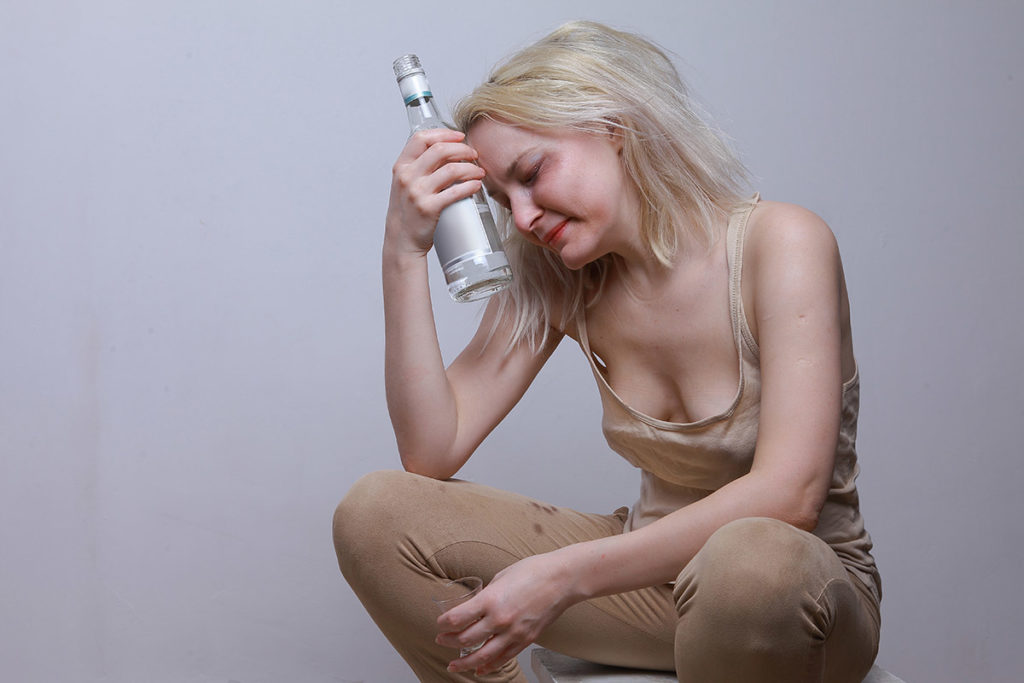 woman resting her head on a liquor bottle experiencing anxiety and alcohol