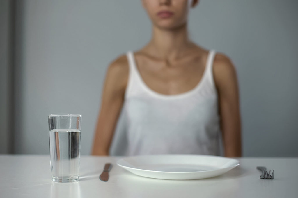 woman sitting before empty plate dealing with trauma and eating disorders