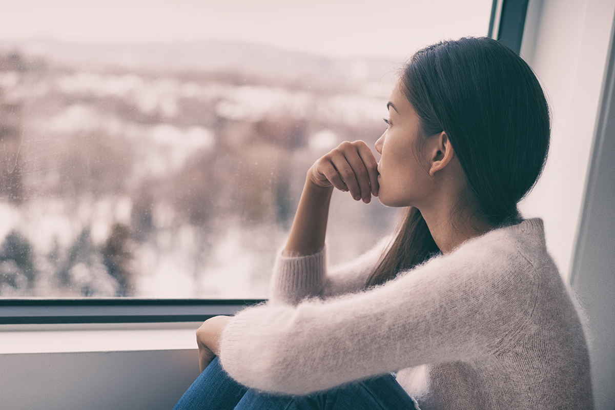 woman looking out window in need of mental health treatment