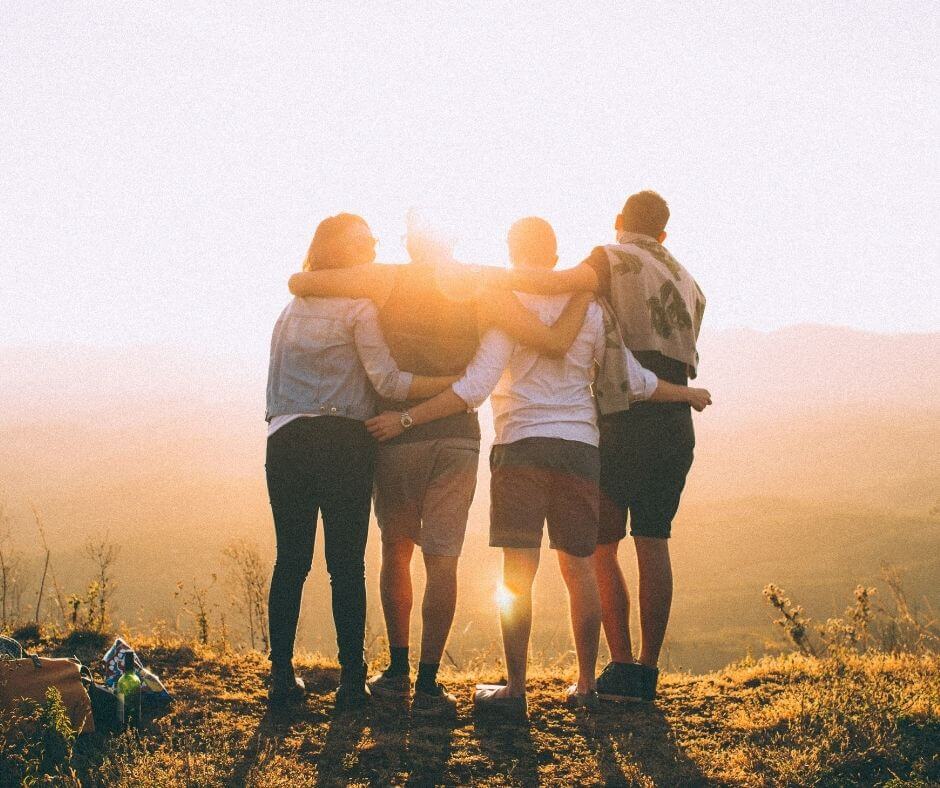 A sunset with 4 people, arms around each other looking at the top of a mountain