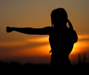 A woman in silhouette punches the air with a sunset behind her