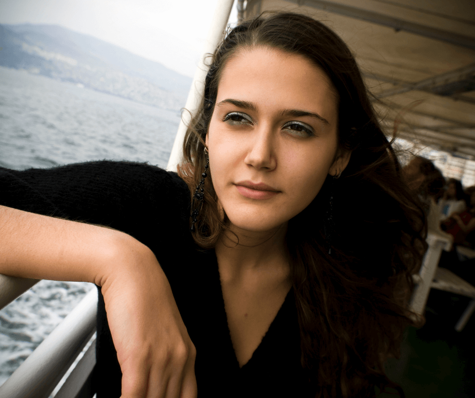 A white woman stares over the railing of a boat over water