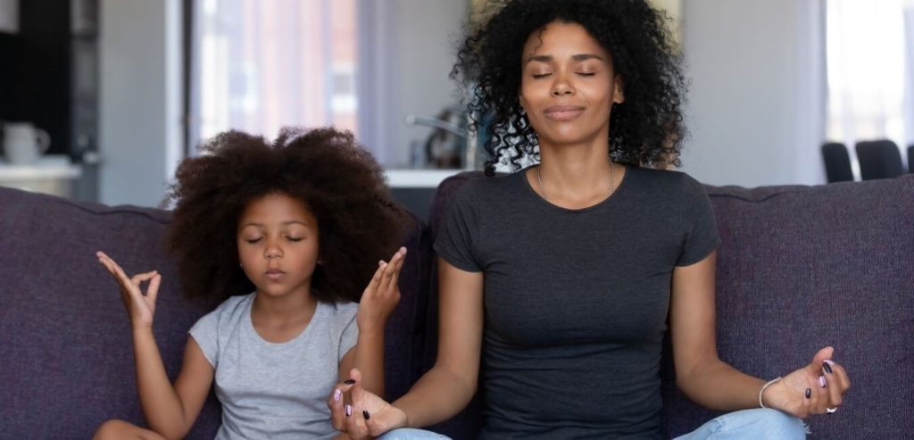 An African American mother and daughter sit on a couch practicing mindfulness