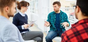 A group therapy session with a female counselor speaking to three young men