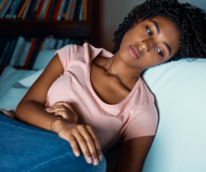 a young black woman in a pink short sleeved top rests her head on a blue couch looking sad