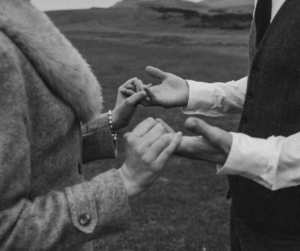 A black and white photo where two people are holding both hands in front of them with their fingers touching, in an intimate way