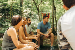 A group of men and women sit outdoors amongst trees.