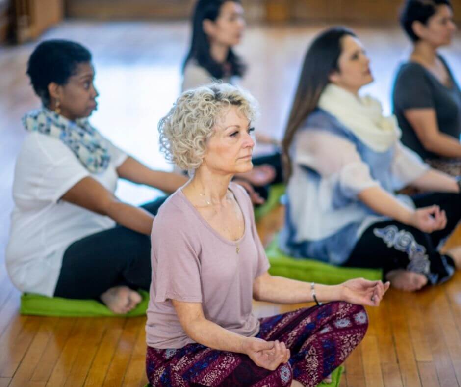 A group of women meditating sitting on a wooden floor