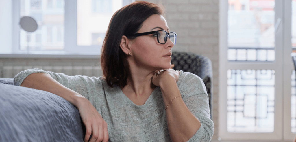 Woman wearing glasses looking away sitting on the floor at house