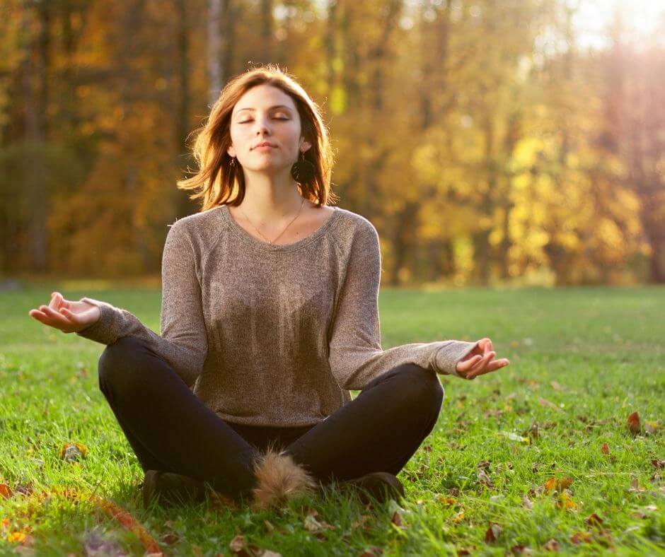 Young woman meditating outdoors sitting on the grass
