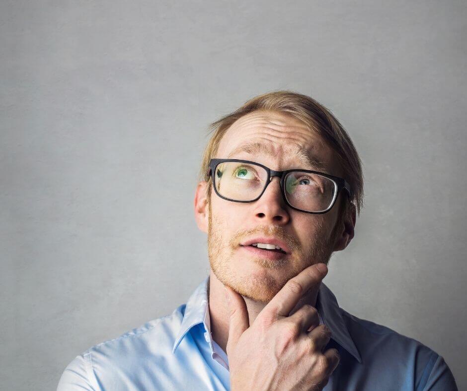 A man with glasses in a blue shirt with his hand on his chin thinking about something