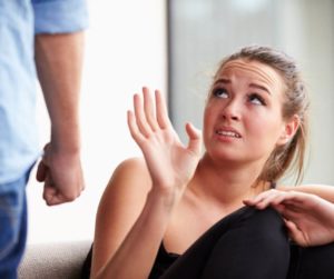 A young blonde woman looks scared and asks a man with a clenched fist not to hit her.jpg