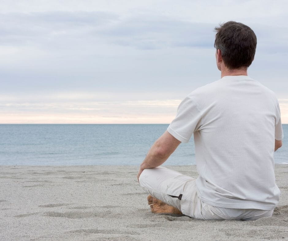 Man sitting cross-legged on a beach meditating