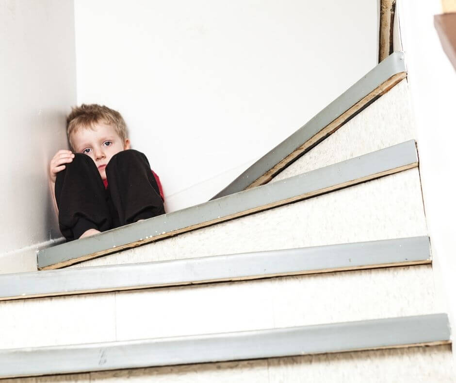 Tiny little boy hiding on the stairs looking very sad and alone