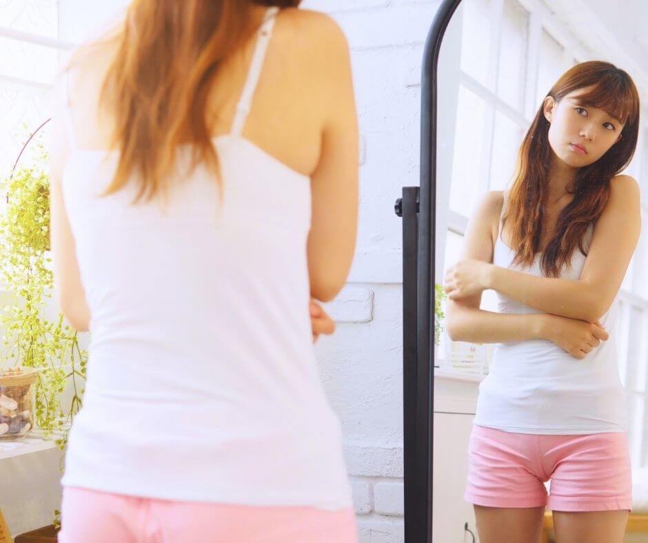 Young woman looking unhappy as she looks at herself in the mirror