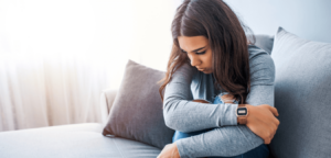 Young woman of color wearing grey sweater sitting on sofa looking depressed