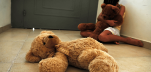 A female child lying on the floor and crying while holding her stuffed toy