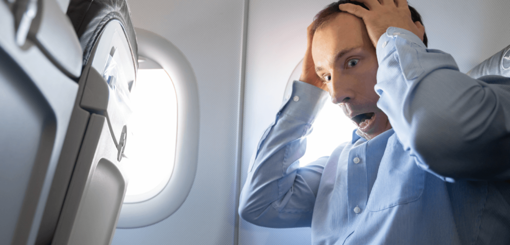 A young man with both hands on his head having anxiety attack inside of a airplane