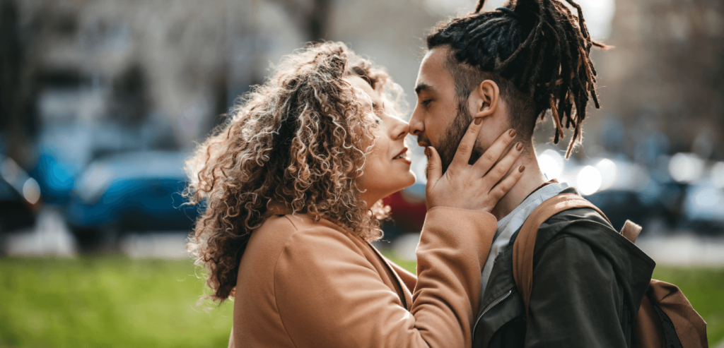 A woman who is holding her partner's face and appropriately kissing it while they are standing on a park