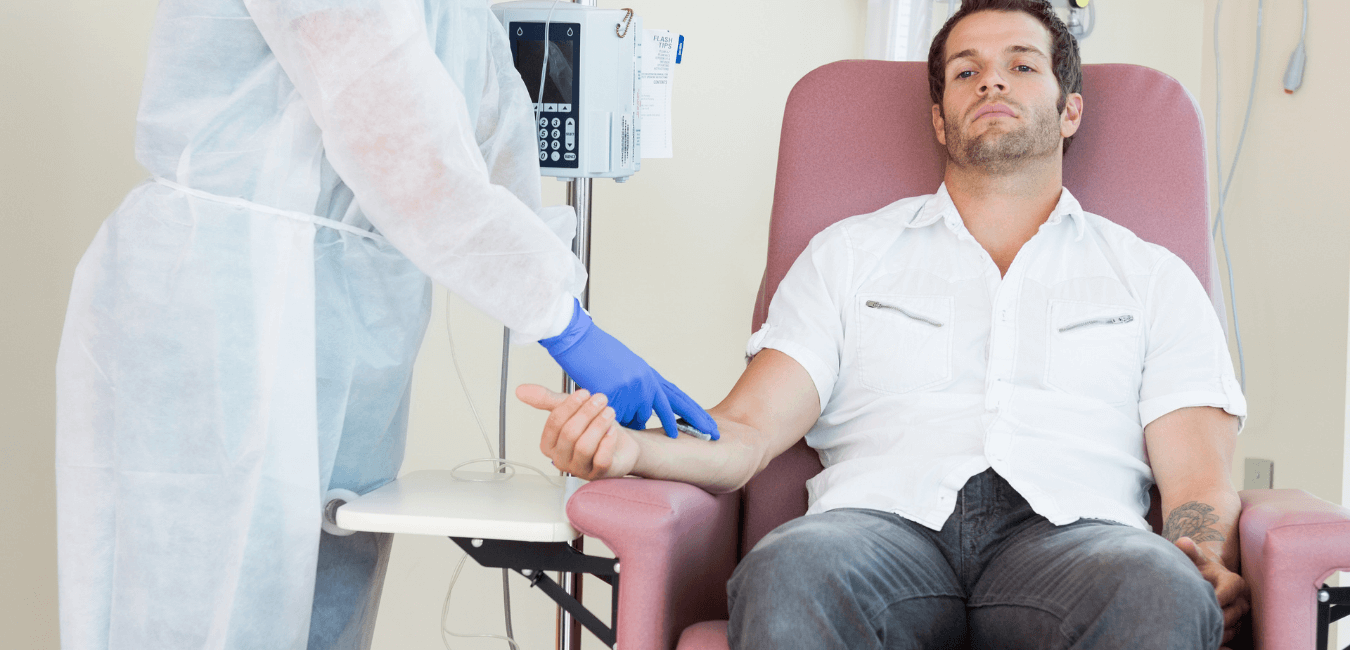 A depressed male sitting on a couch of a treatment facility while being administered medication by a healthcare professional