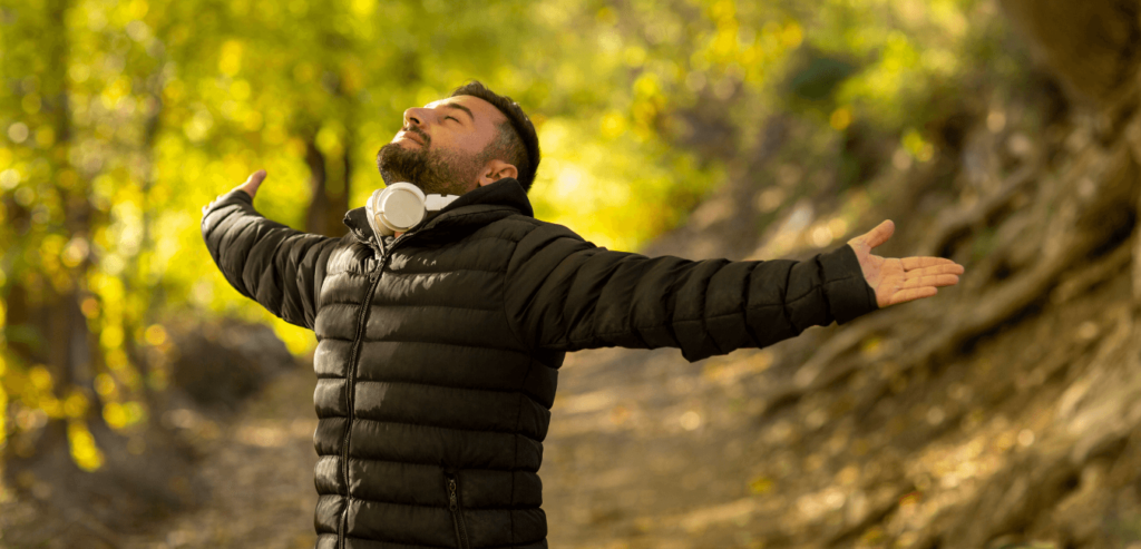 Man wearing black jacket standing outdoors deep breathing with arms wide open