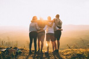 four person hands wrap around shoulders while looking at sunset, these friends support each other through Embracing Holistic Substance Abuse Treatment