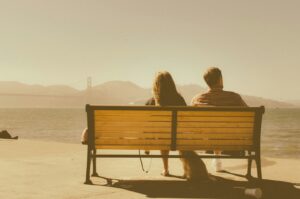 man and woman sitting on bench beside body of water, evaluating signs of codependent relationships