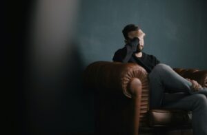 a man holds his head while sitting on a sofa, coping skills for substance abuse
