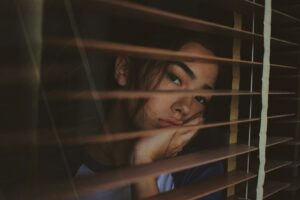 a woman looking out of a window with blinds, struggling with bipolar and eating disorders