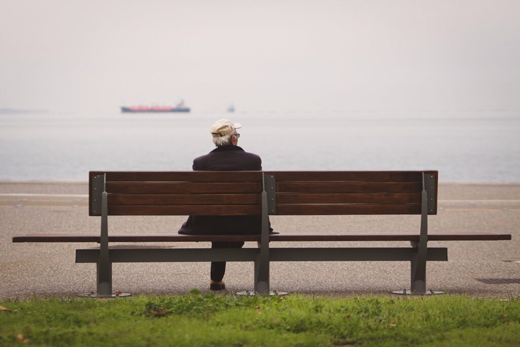 man sitting on brown bench facing on the sea struggling with fear of intimacy