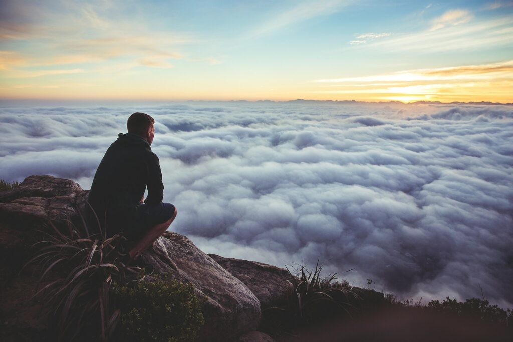 man sitting on gray rock while staring at white clouds thinking about alcohol assessment