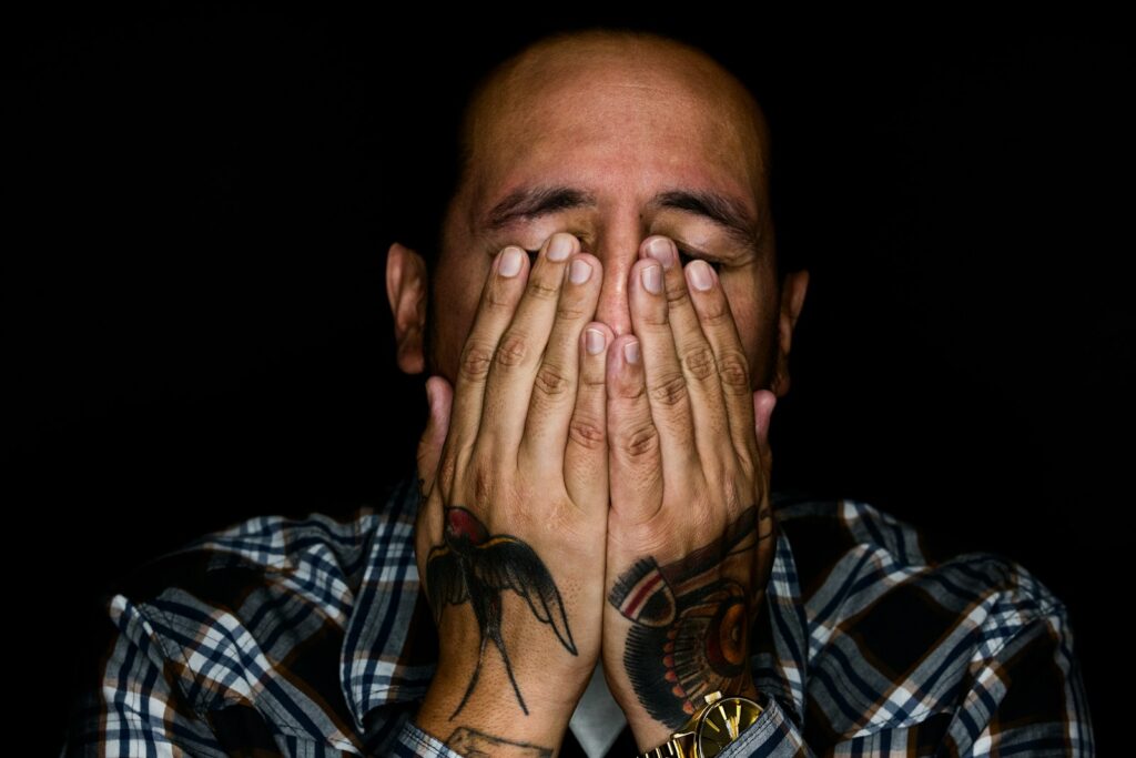 man wearing black, white, and gray plaid sport shirt covering his face, grief and substance abuse