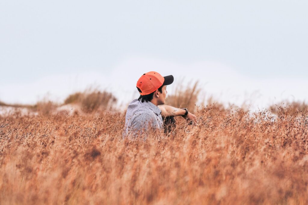 sitting man wearing red cap on brown flower field at daytime wresting with the thought that adverse childhood experiences can have an impact on his life