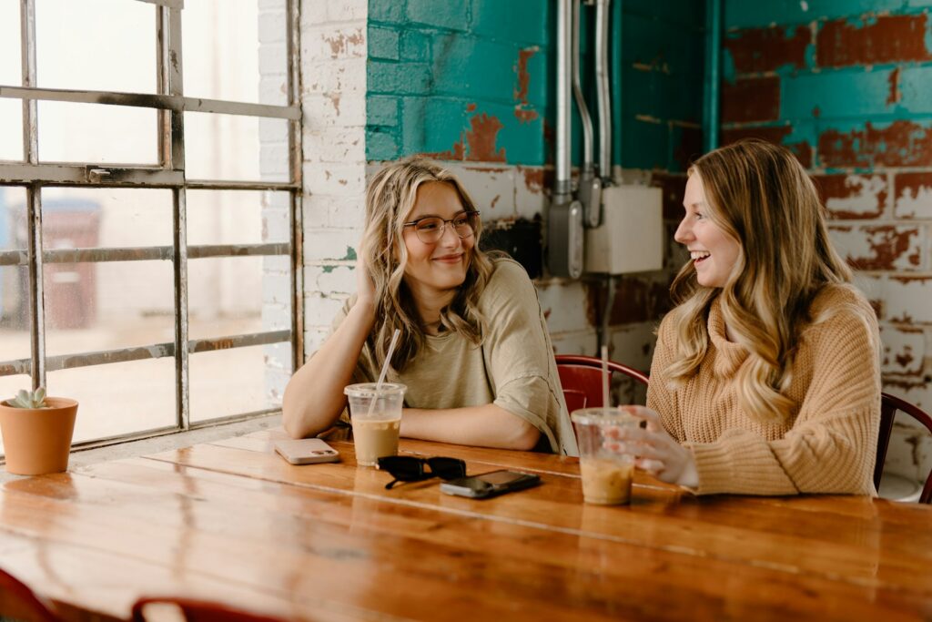 a couple of women sitting at a wooden table practicing coping skills for trauma