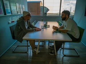 man in black jacket sitting beside man in gray jacket, embracing honesty in recovery