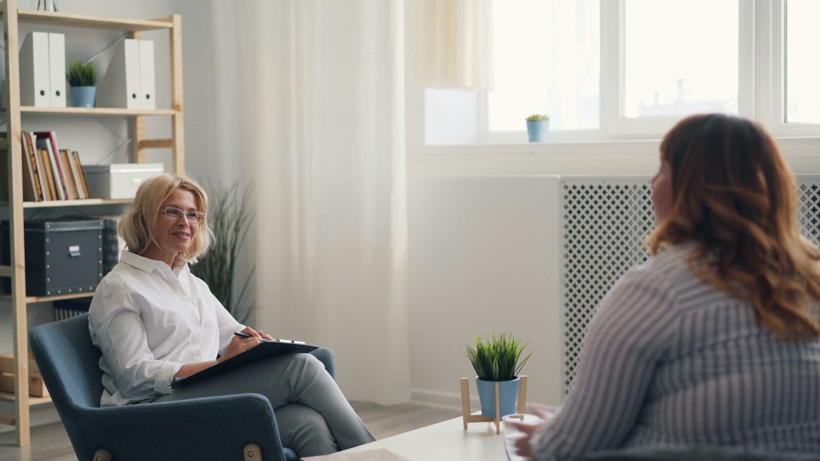 a woman sitting in Blue Cross Blue Shield mental health treatment in a chair talking to another woman