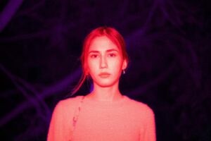 A woman addicted to sexting in a pink sweater lit by vibrant red and purple light