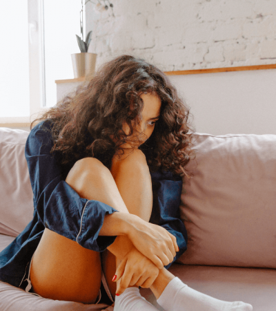 Young woman of color sitting on couch in home looking unhappy